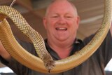 A smiling man holds a large snake.