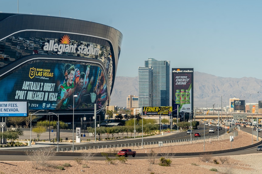 Advertising for rugby league is displayed on Allegiant Stadium near a main highway in Las Vegas