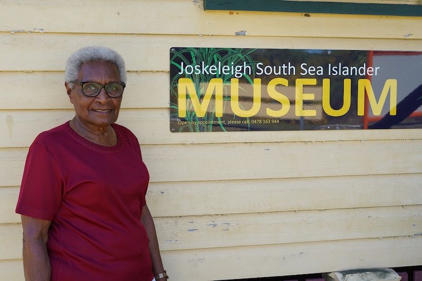 Aunty Doris standing, smiling in front of a sign that says Joskeleigh South Sea Islander Museum.