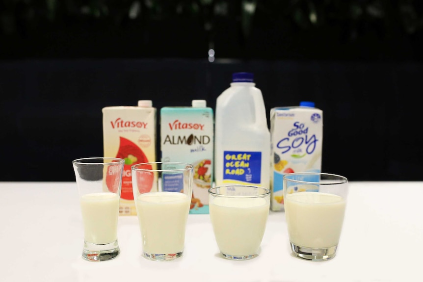 Glasses of cows milk, soy milk and almond milk in front of their containers.