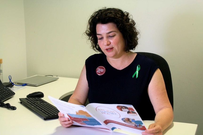 Ms Harvey sits at a desk reading a brochure.