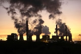 The silhouette of a smoking gas plant is contrasted against a golden sunset. 