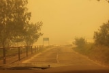 Sign of Happy Valley in the distance as car drives towards the smoke-covered beach.