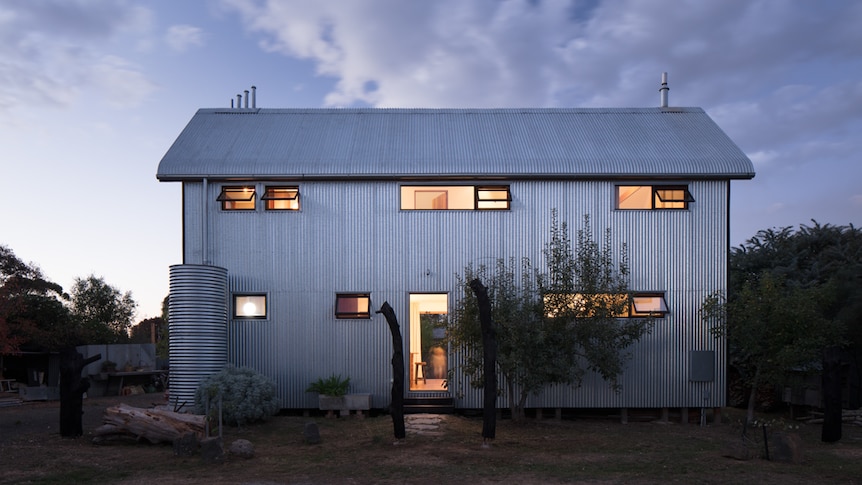 A two-storey house with galvanised steel cladding, photographed at twilight.