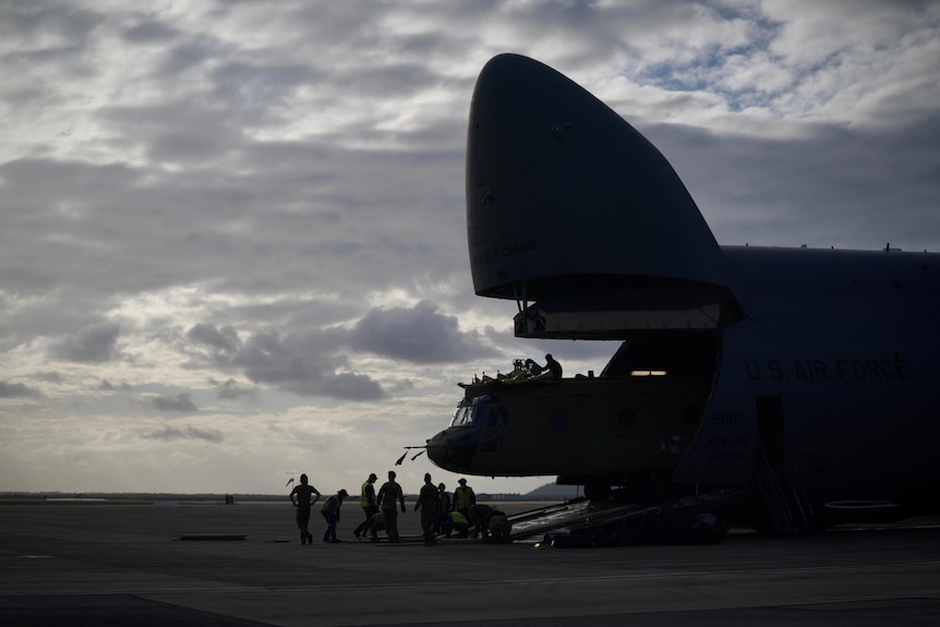 A Chinook helicopter is unloaded from a large military transport plane