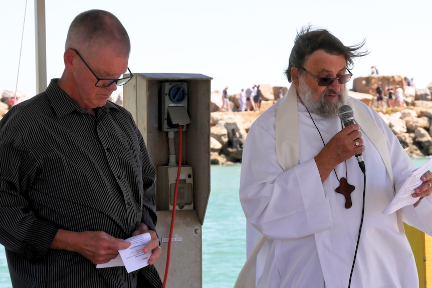 Two men speaking to a crowd on a jetty 