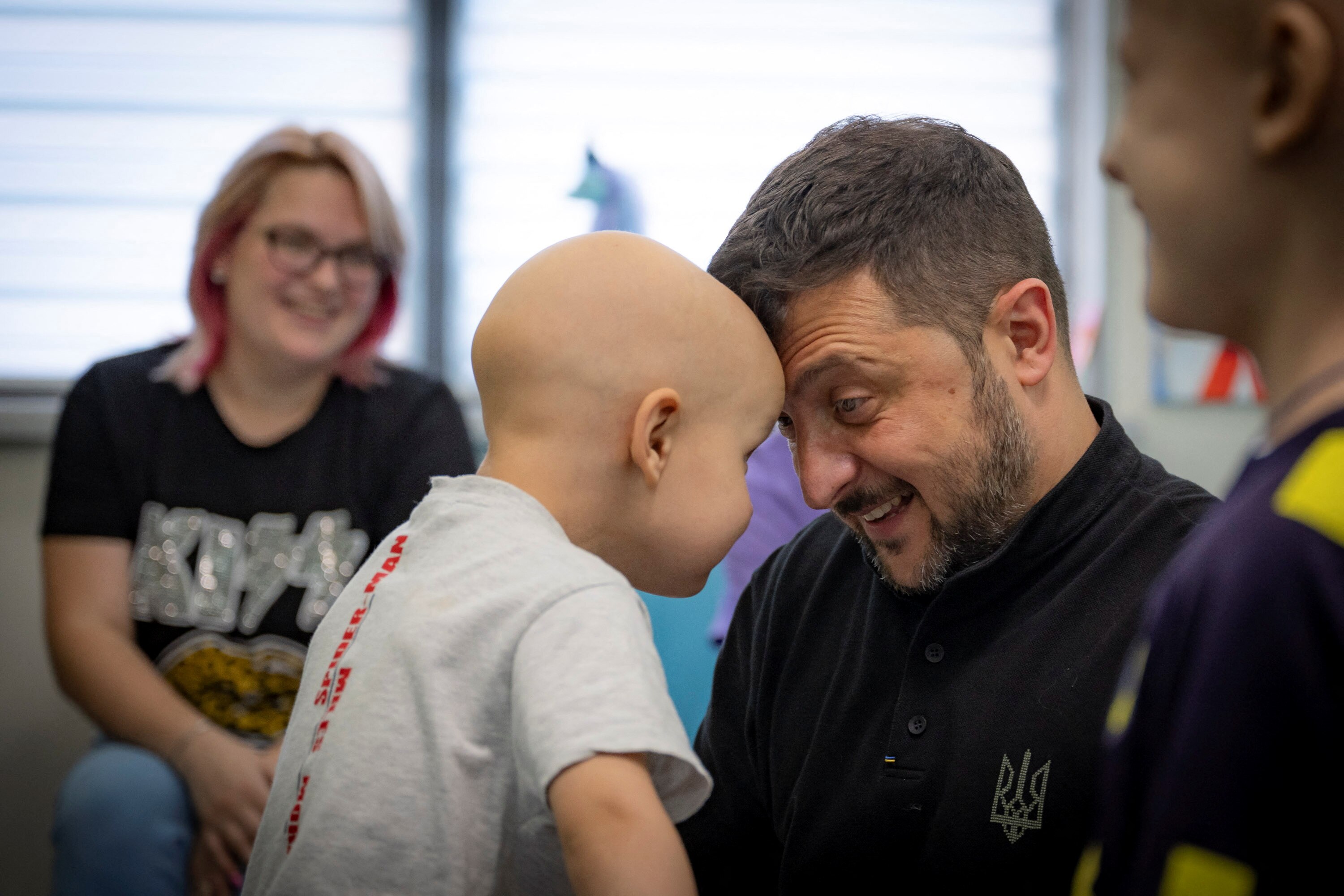 A young bald child holds his head up and touches the forehead of a man who is smiling