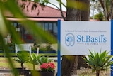 A blue and white sign that reads 'St Basils Victoria' in front of a building