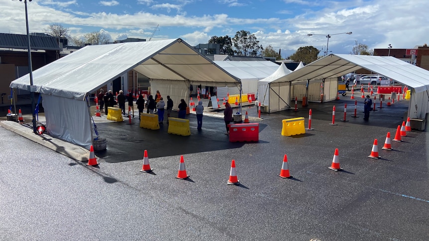 White tents and traffic cones mark a COVID-19 testing site where people are lining up.