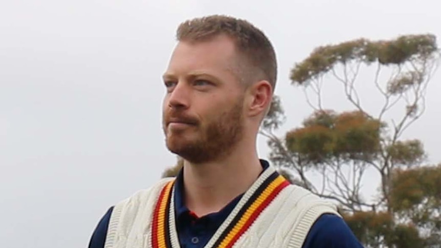 A man stands in cricket whites with his hands behind his back.