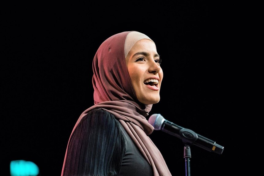 A woman wearing hijab standing behind a microphone
