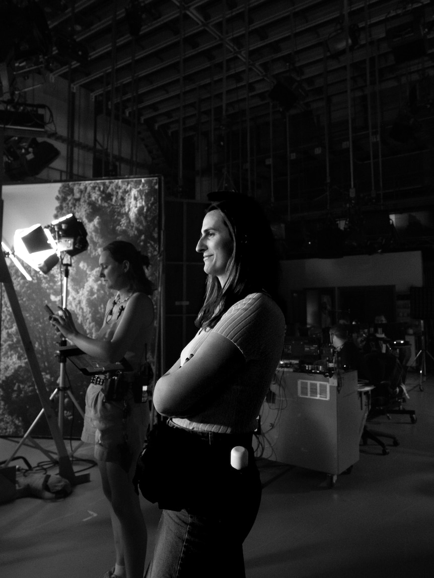 A black and white image of Bayley Turner, a trans woman, working on a film set. She has her arms folded and is smiling slightly.