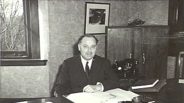A historic photo of a man in a suit sitting at an office desk