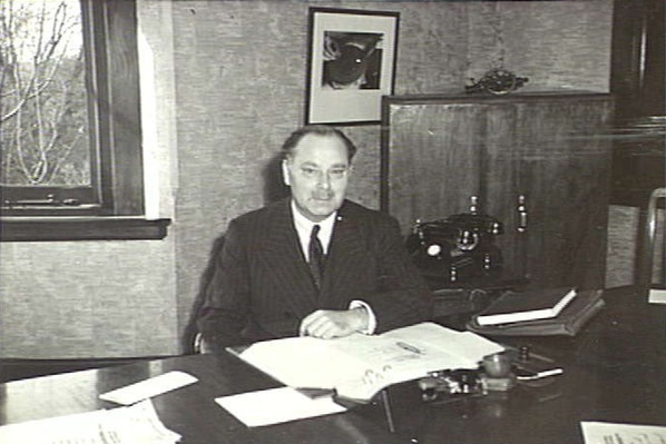 A historic photo of a man in a suit sitting at an office desk