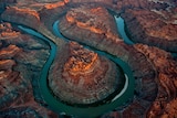 A bird's eye shot of a deep teal river that has carved loop-like shapes into a rugged orange landscape.