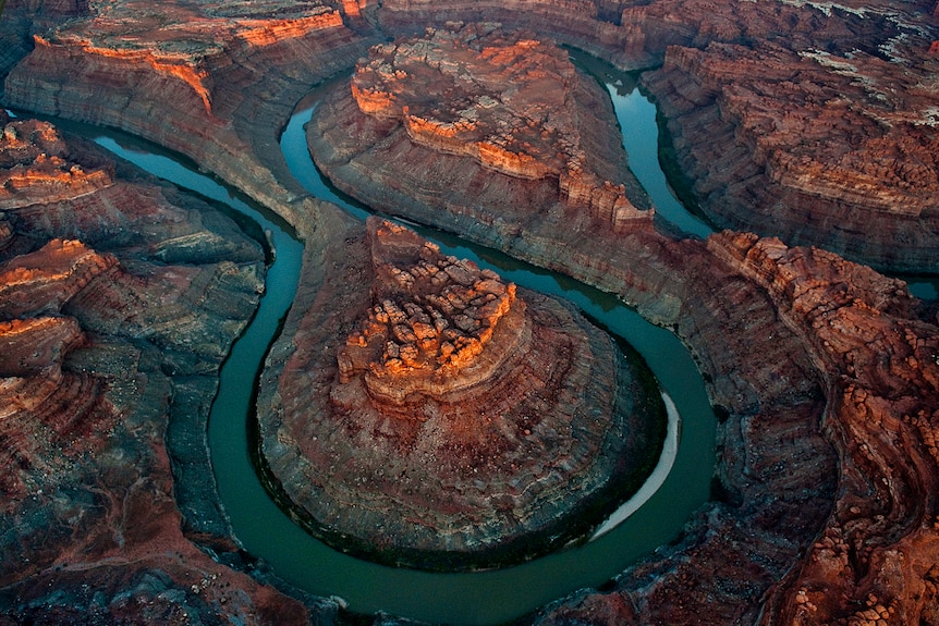 A bird's eye shot of a deep teal river that has carved loop-like shapes into a rugged orange landscape.