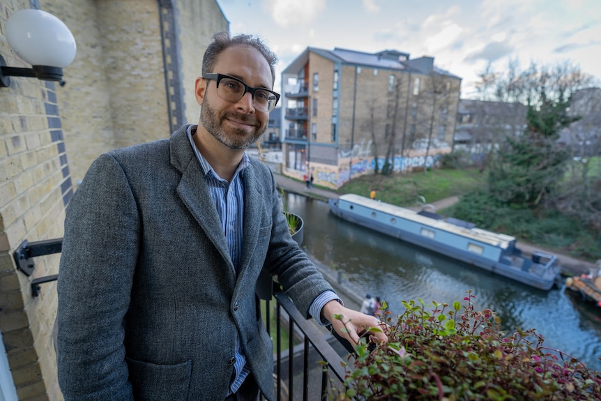 White man with glasses standing on a balcony in London, with a canal below in the background