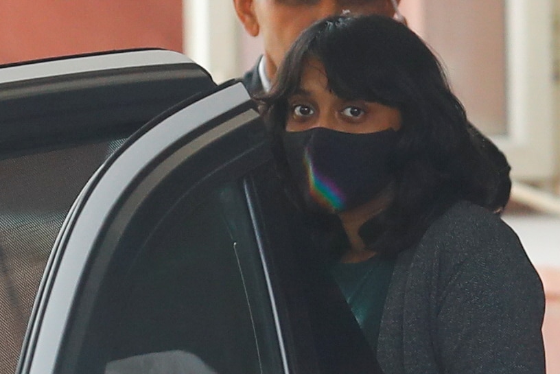 A woman wearing a facemask is getting into a car.