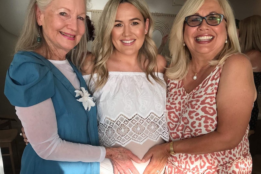 Mother-in-law Helen Bertolini and mother Vicki Fleming with their hands on a pregnant Sarah Bertolini's stomach.