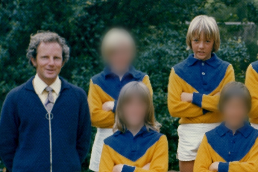 Glen Fearnett stands in a group photo with an unhappy look on his face and his arms folded.