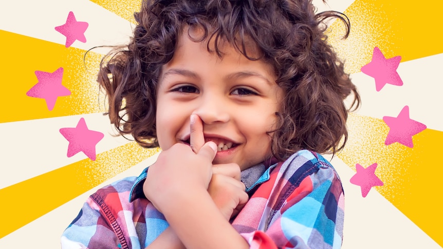 Preschool-aged boy grins cheekily with hand partially covering his mouth