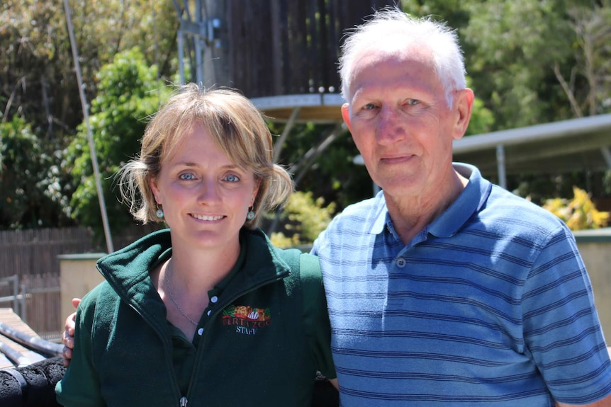 A woman and man stand next to each other outdoors at a zoo.