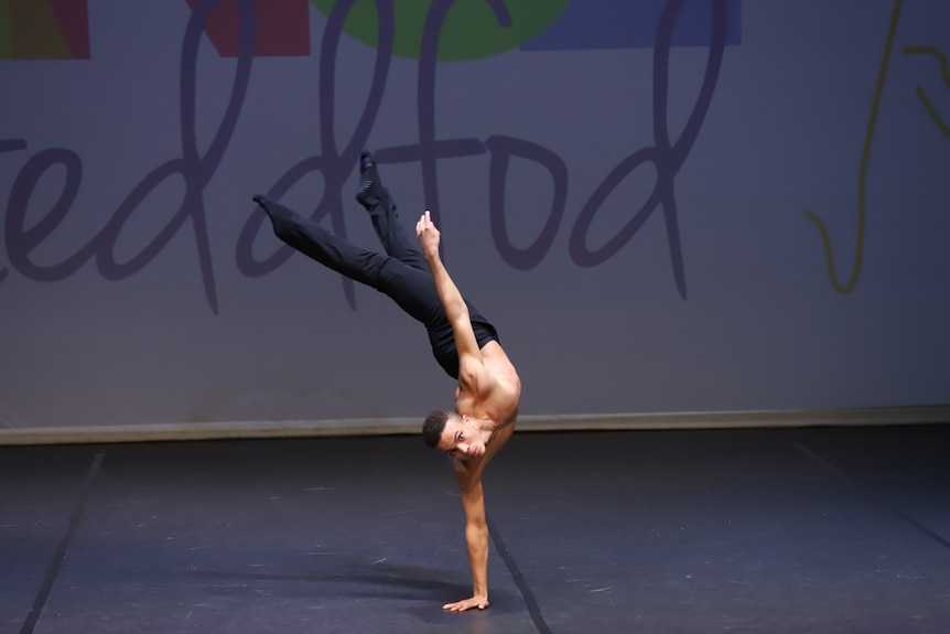 A young dancer holds himself up on one hand while performing on stage 