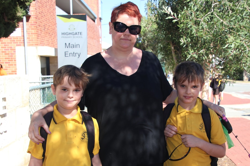A mother stands outside school with her two young sons posing for a group photo.