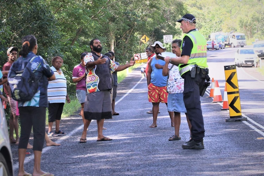 A group of residents from Yarrabah stand on a road checkpoint with a Queensland police officer.
