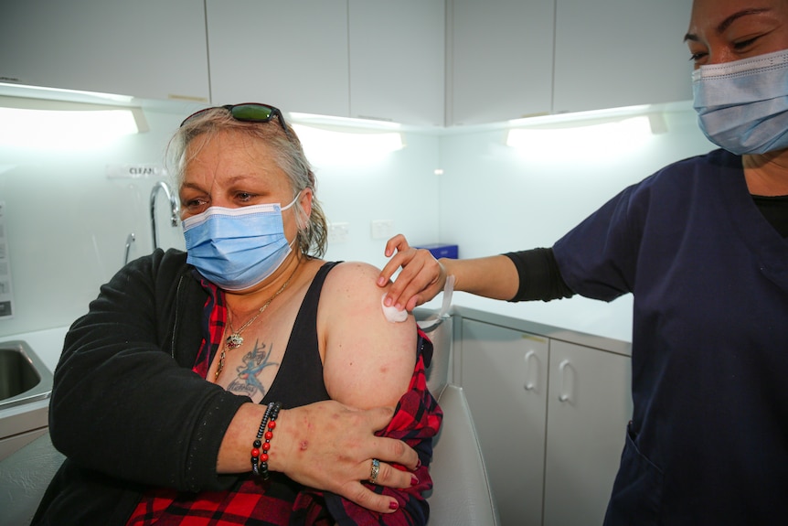 A woman wearing a mask holds her shirt after getting a COVID-19 vaccination.