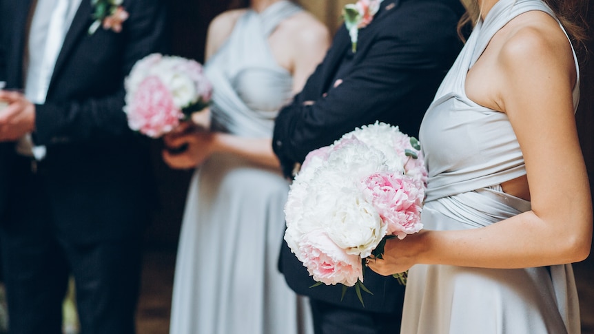 close up of bridesmaid holding flowers at a wedding with bridal party in the background