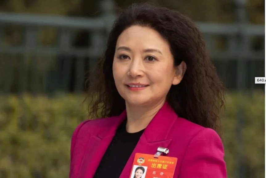 A woman in a dark pink jacket with a photo id pinned to her lapel.