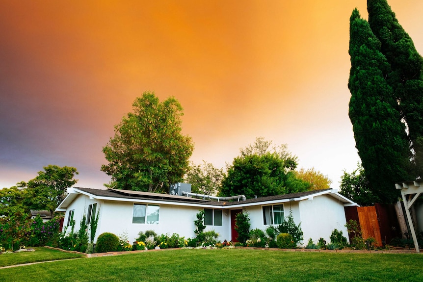 A single-storey white house with a neat yard, with a setting sky in the background.