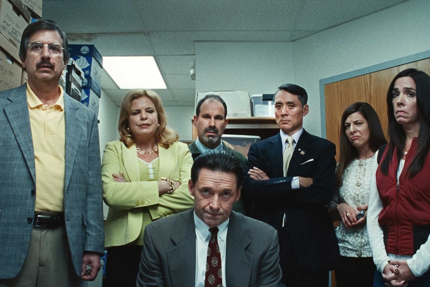 Hugh Jackman, Ray Romano and other actors gather together in office-wear in an office in the film Bad Education