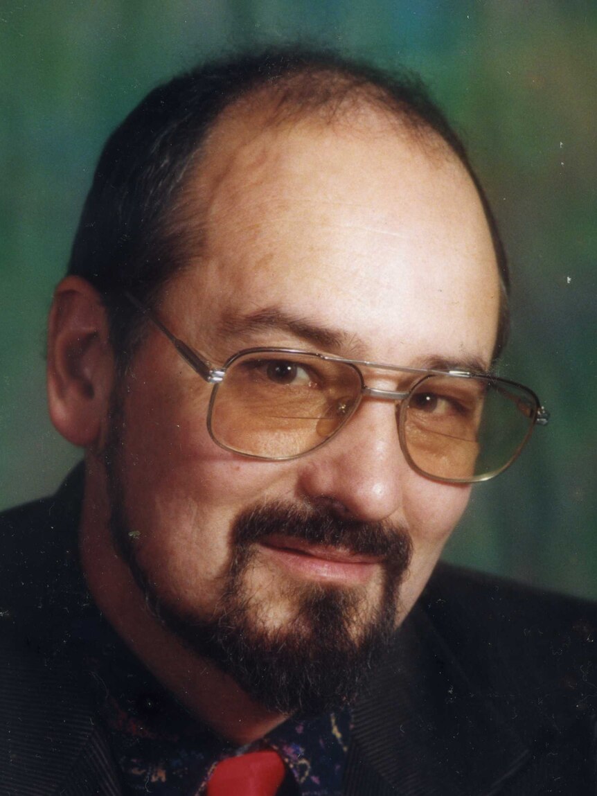 Headshot of a man with brown hair and glasses wearing a red and white tie.