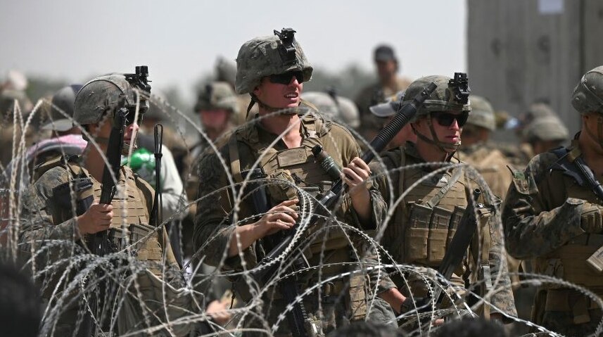 US soldiers stand guard behind barbed wire as Afghans sit on a roadside near the military part of the airport in Kabul