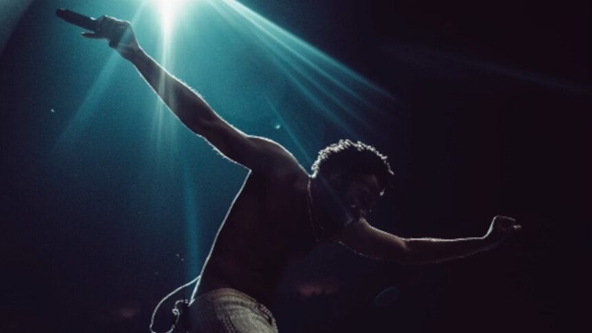 Backlit photo of Childish Gambino performing shirtless under a teal blue stage light