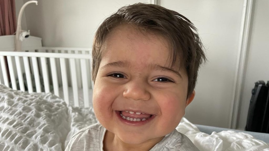 A little boy wearing white and smiling.