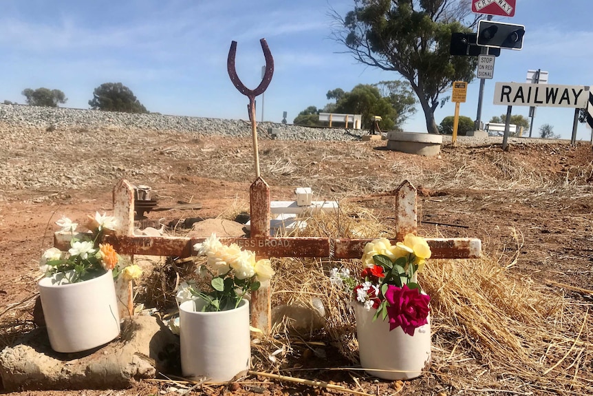 A memorial with a horse shoe and flowers beside Yarramony Road rail crossing