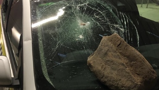 A large rock sits on the windscreen of a police car. The windscreen is shattered.