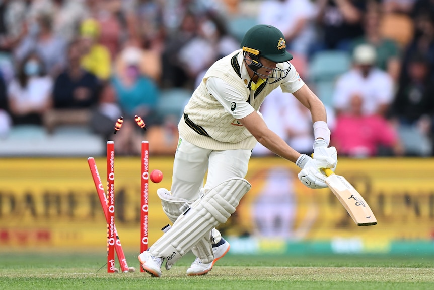 Marnus Labuschagne falls as his stumps are broken by a pink cricket ball behind him