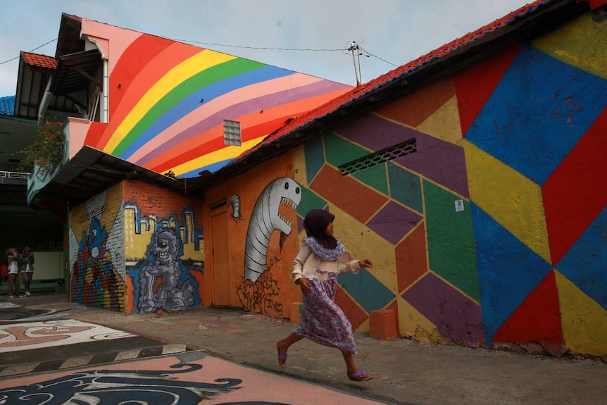 A girl running in front of a colourful mural in Wonosari Village, Indonesia.