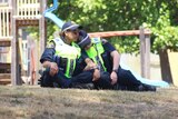 Two police officers sit on the ground, with one of them leaning on the other.