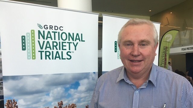 A man wearing a blue button up shirt standing in front of a banner that says 'GRDC'.