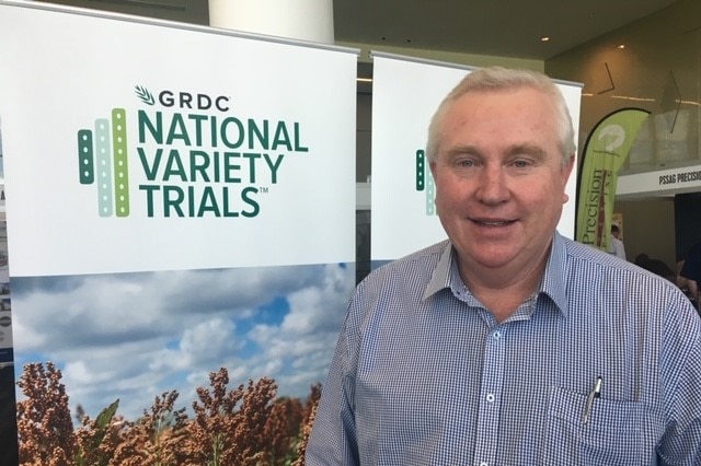 A man wearing a blue button up shirt standing in front of a banner that says 'GRDC' National Variety Trials.