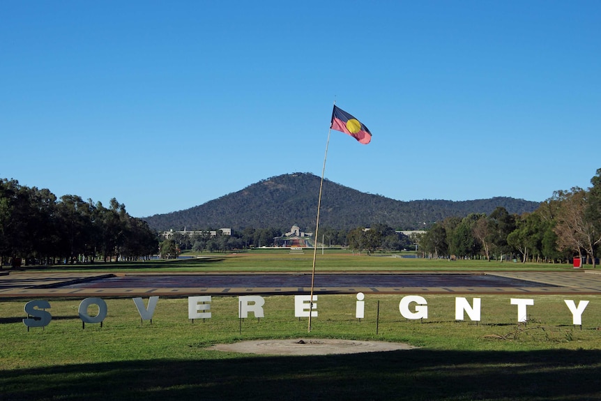 A sign reading sovereignty stuck in grass outside Canberra's Old Parliament House, in front of the Aboriginal flag.