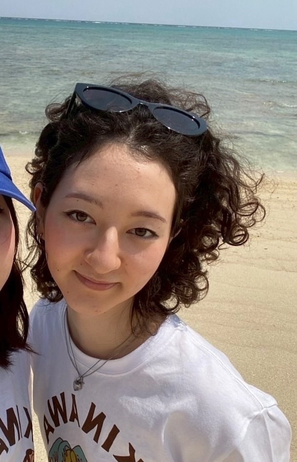 A woman with black curly hair smiles while standing on a beach