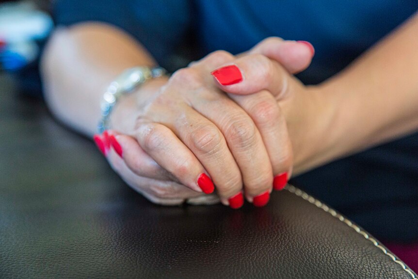 Close up of a woman's clasped hands with bright red nail polish.