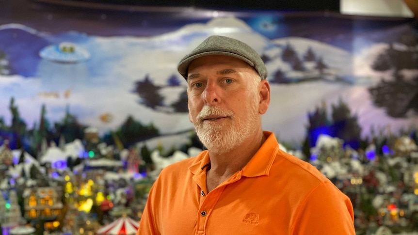 Older man stands in front of miniature Christmas village.