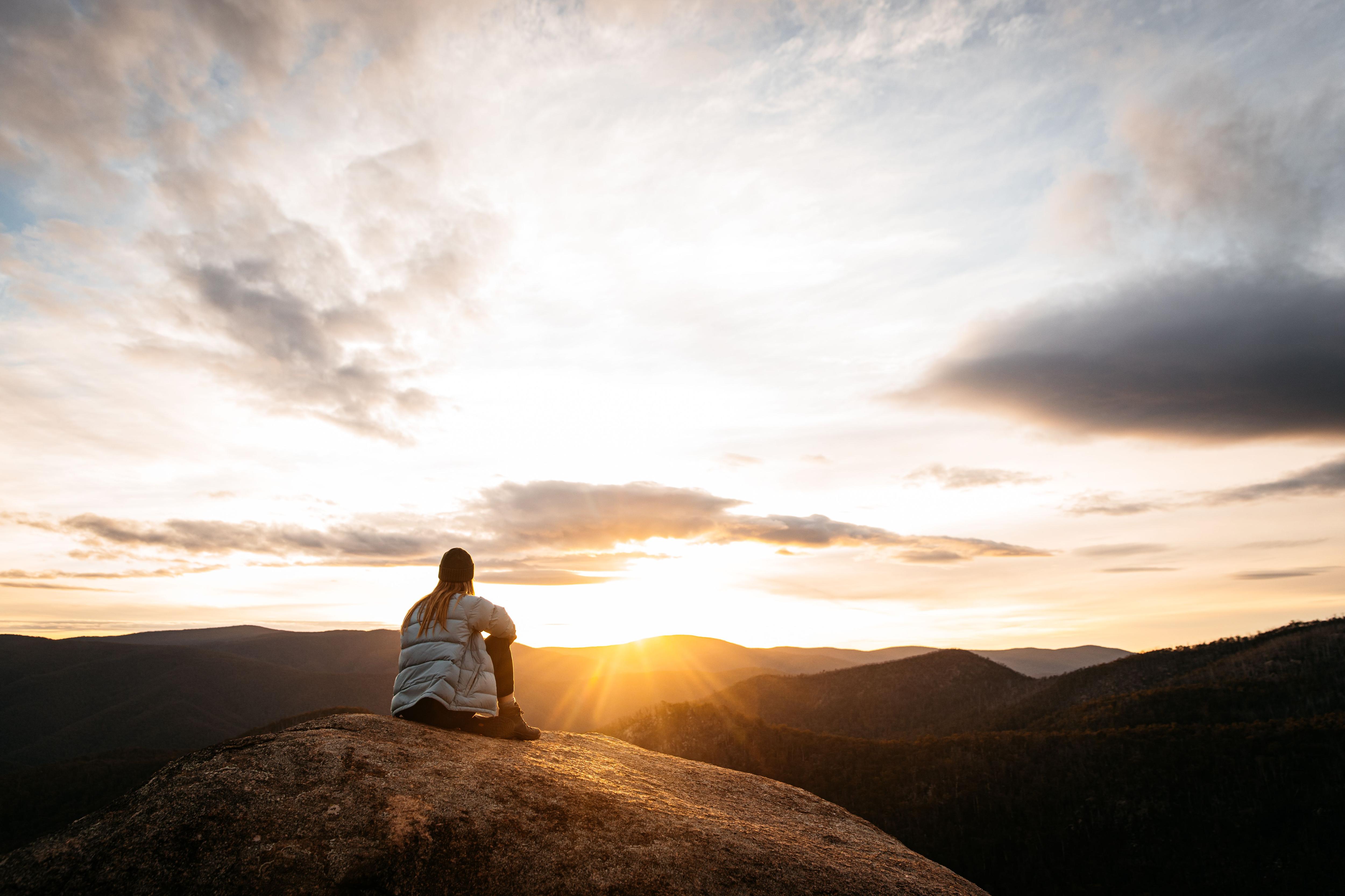 Woman sitting on a rock in the mountains looking at the sunset